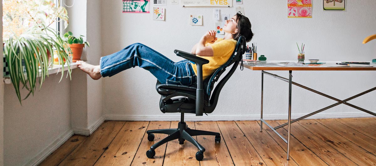La ilustradora, pintora y autora Molly Rose Dyson en su estudio, sentada reclinada en una silla gaming Embody en negro y azul cian