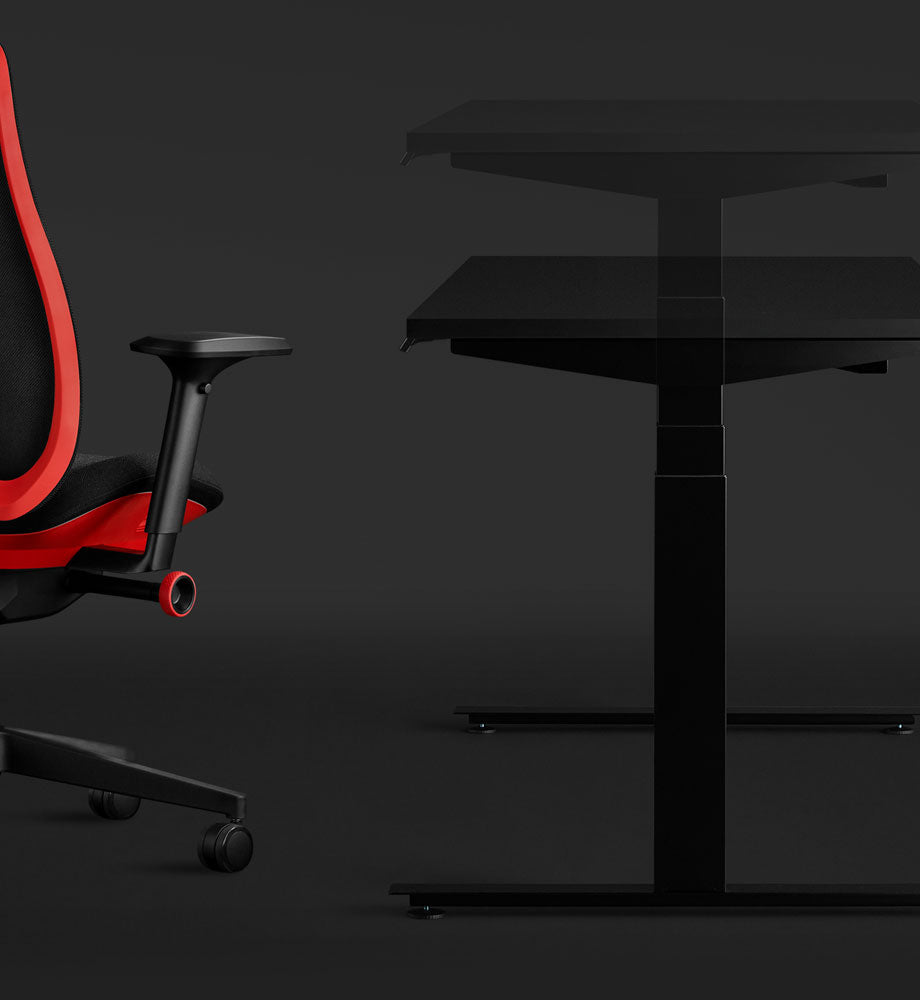 Vista lateral de una mesa de juego Nevi negra y una silla de juego Vantum roja de Herman Miller, en la que se destaca el elemento de bipedestación de la mesa.