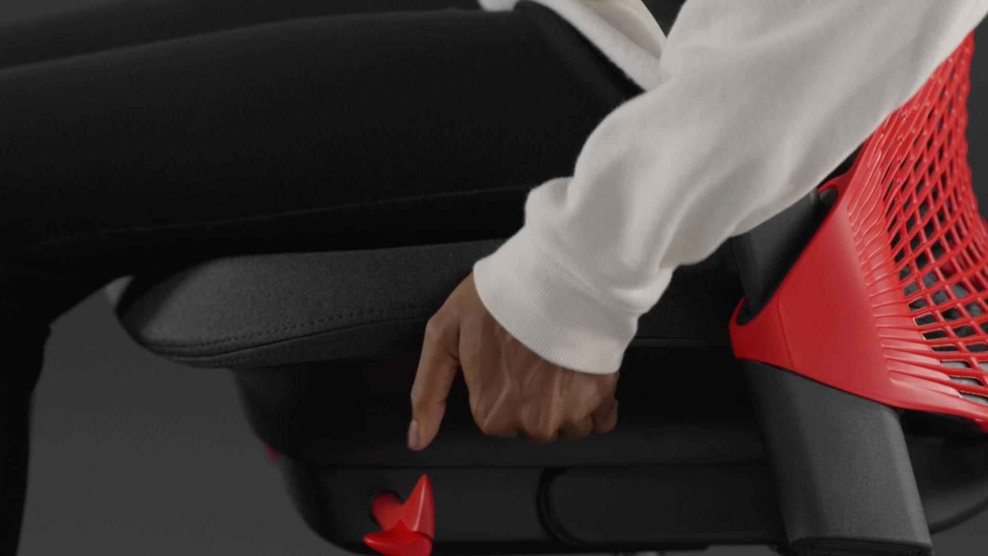 Vídeo de una persona sentada en una silla de juego Sayl roja y negra de Herman Miller, acercándose a la silla para ajustar la profundidad del asiento.