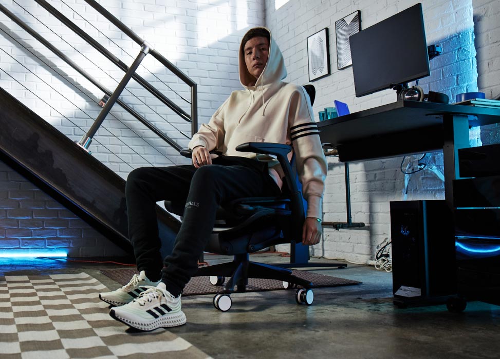 Foto de Jelty, del equipo G2 Esports, sentado en la silla G2 Embody con la espalda hacia el equipo de gaming, que incluye el escritorio Nevi en negro con monitores Ollin.