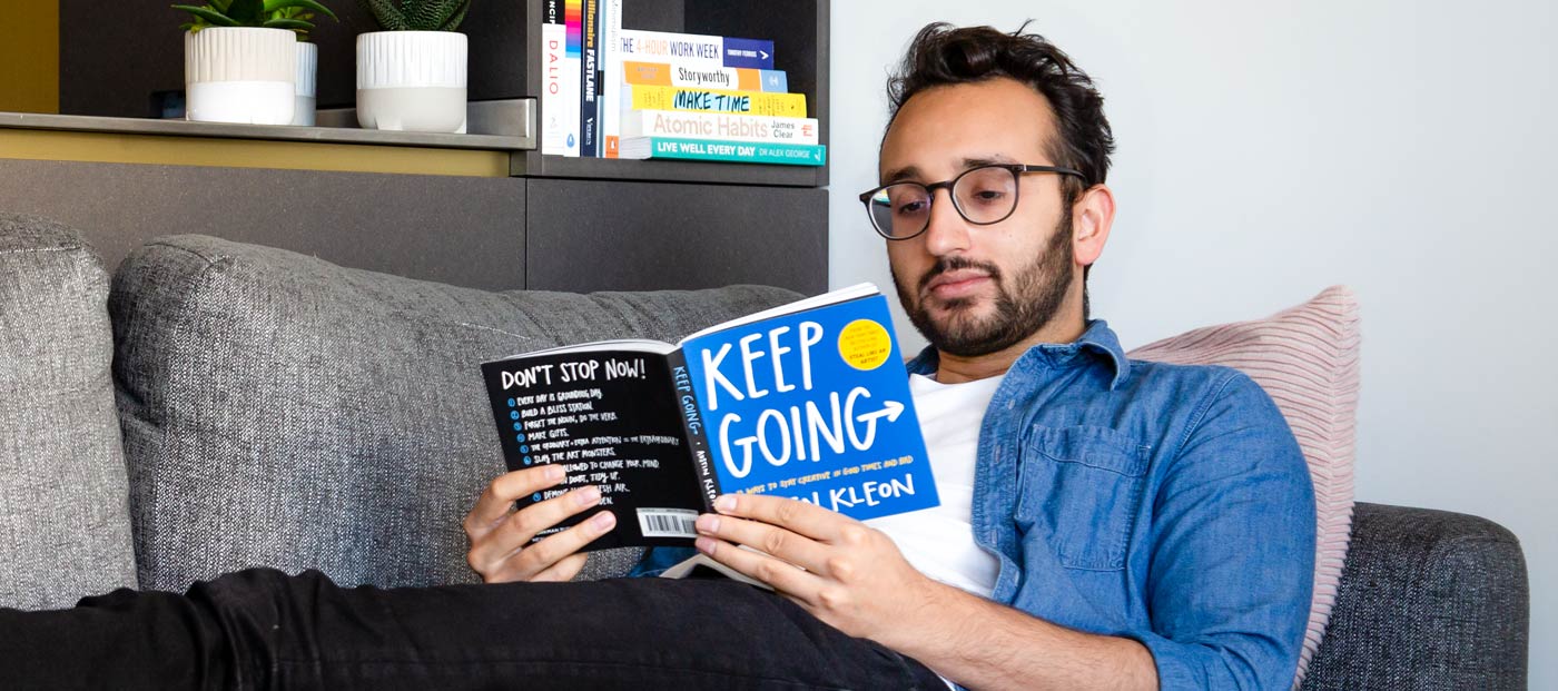 Foto de Ali Abdaal tumbado en el sofá leyendo un libro titulado Keep Going