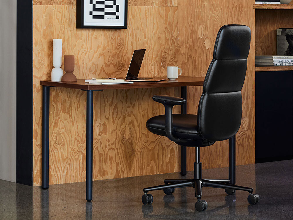 Una silla de oficina Asari negra frente a un escritorio OE1 negro y de nogal en un interior con un diseño moderno de mediados de siglo.