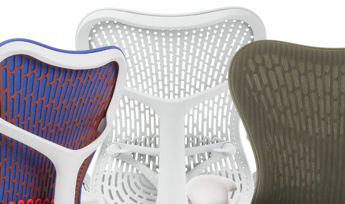 Primer plano de tres sillas de oficina Mirra 2 de Herman Miller, mostrando la gama de colores disponibles. La primera es azul, naranja y blanca, la segunda es sólo blanca y la tercera es verde.