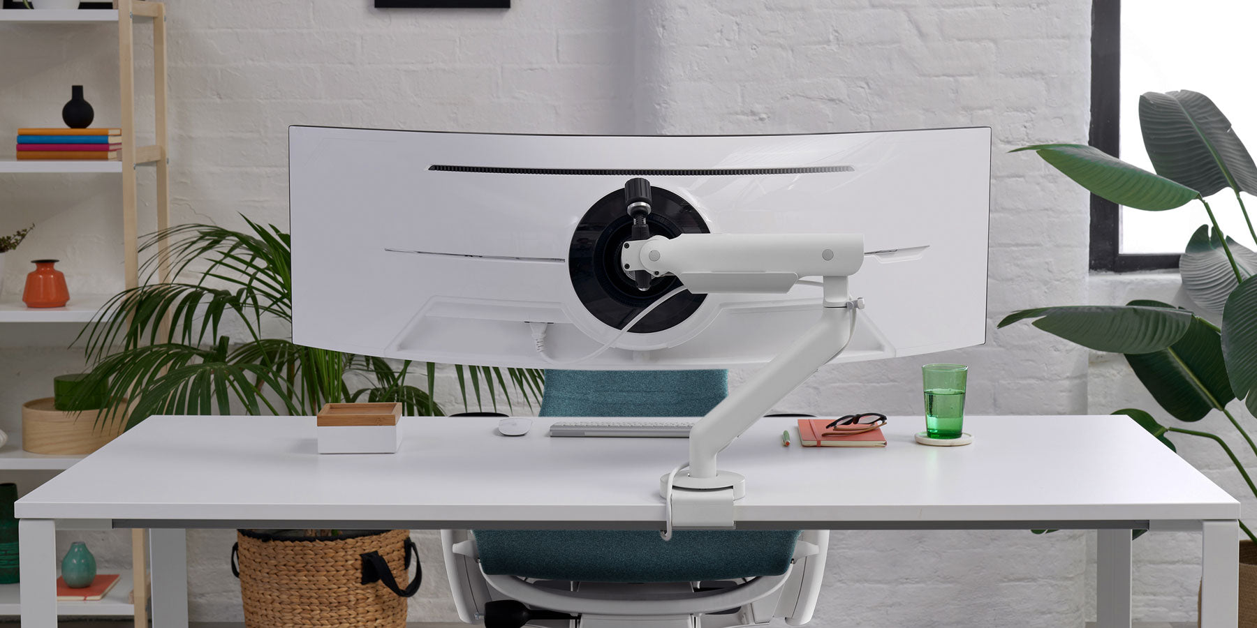 Vista frontal de un brazo para monitor Flo X blanco de CBS acoplado a un escritorio blanco, colocado delante de una silla de oficina Aeron negra de Herman Miller.