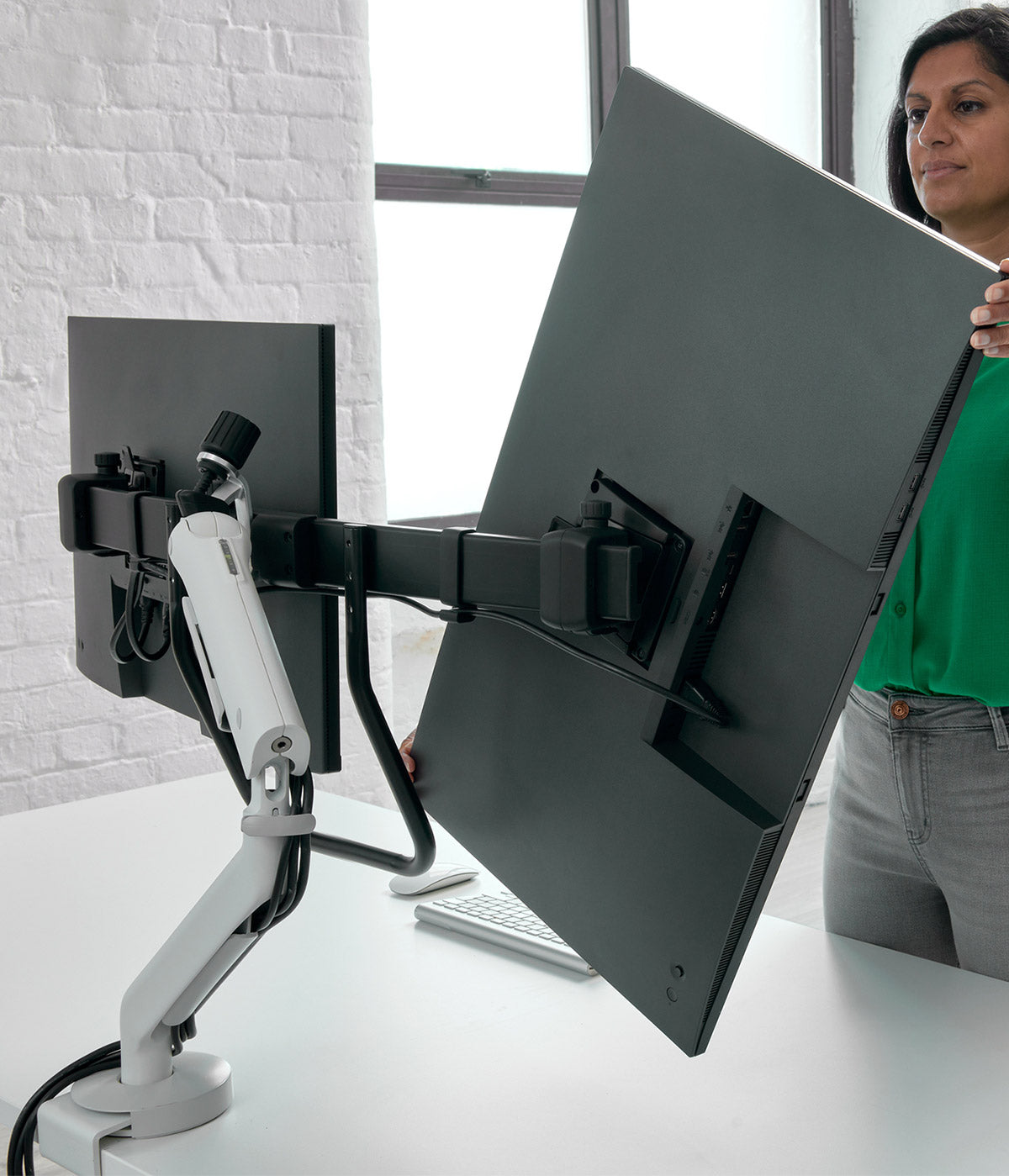 Un brazo para monitor de gran formato CBS Flo X que sostiene dos pantallas mientras un usuario ajusta su orientación.