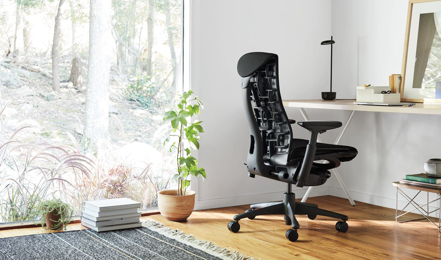 Una silla de oficina Embody negra de Herman Miller, situada en un entorno interior. El espacio incorpora elementos como muebles, suelos y elementos decorativos como una maceta y un jarrón.