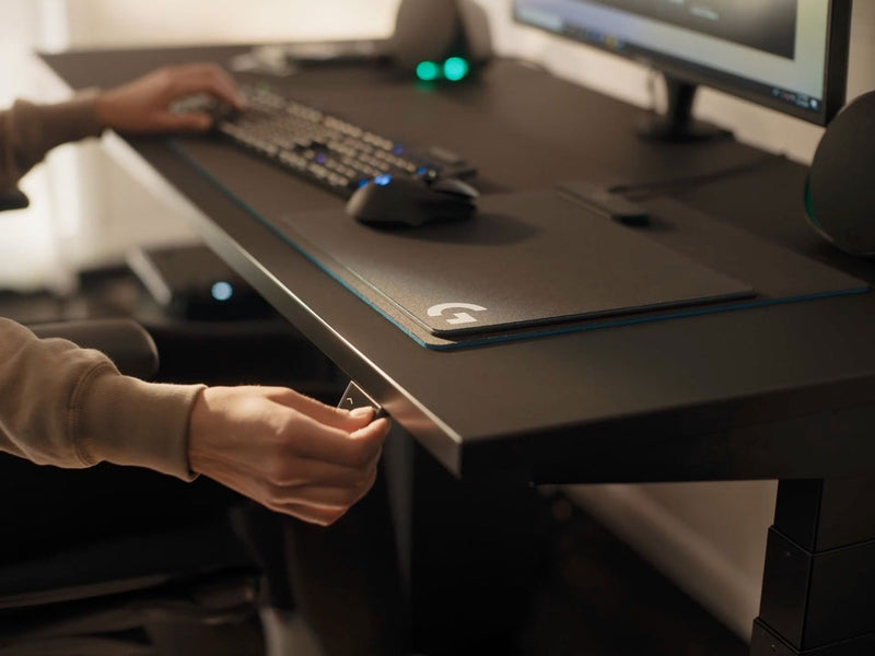 Vídeo de una persona sentada en un escritorio para juegos Nevi negro de Herman Miller, pulsando un botón para bajar el escritorio.