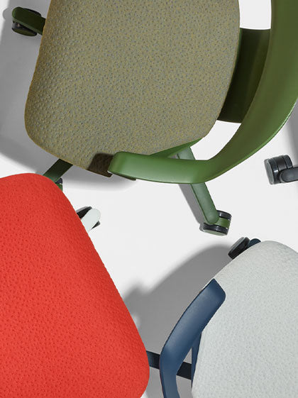 Vista superior de tres sillas de oficina Zeph de Herman Miller en verde, rojo y azul, mostrando la textura de los cojines del asiento.