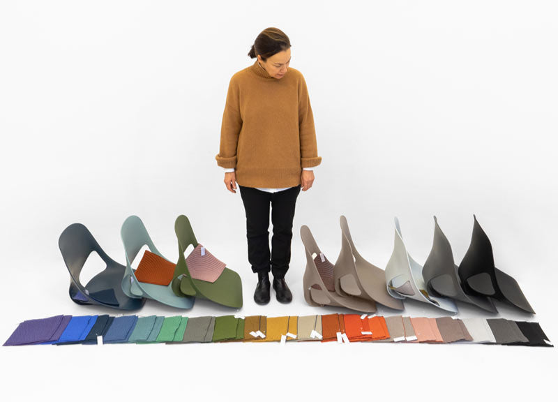 Una mujer de pie junto a varios componentes de la silla de oficina Zeph, con una gama de colores de tela colocados delante.