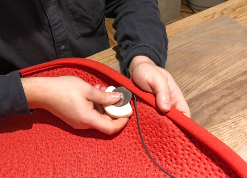 Una persona fabrica un cojín de asiento de tela roja para una silla de oficina Herman Miller Zeph.