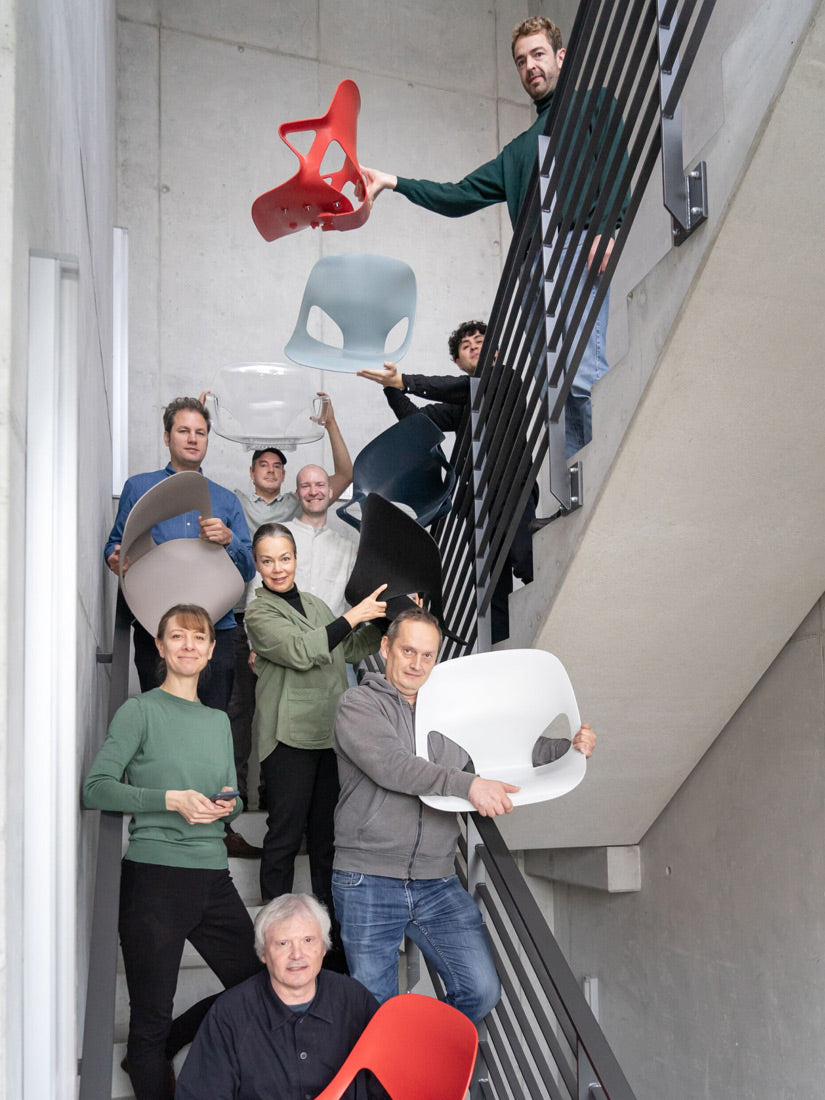 Fotografía de los miembros del equipo de diseño del Studio 7.5 en una escalera, algunos de ellos sosteniendo diversas piezas de la silla Herman Zeph que han diseñado.