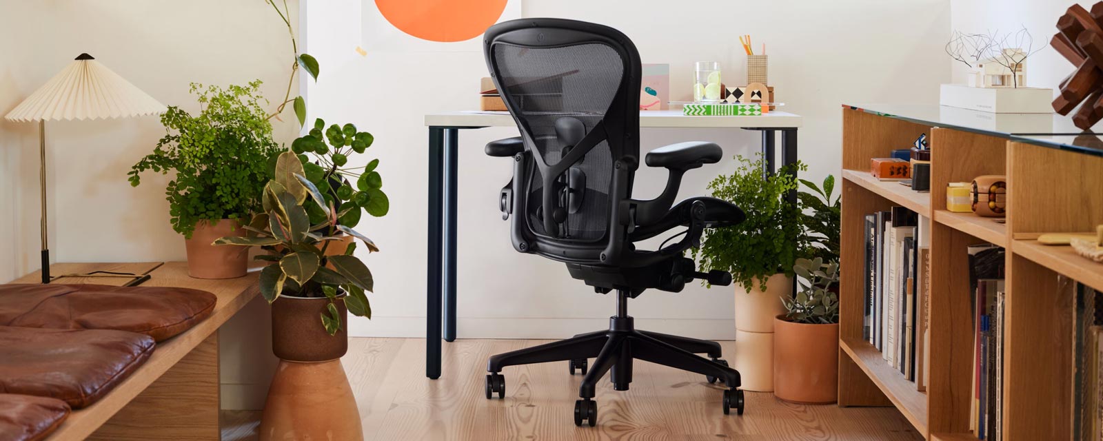 Oficina en casa con la icónica silla de oficina Aeron en color negro delante de un pequeño escritorio OE1 con patas azules y tablero blanco; la habitación también cuenta con una lámpara de mesa Hay Matin
