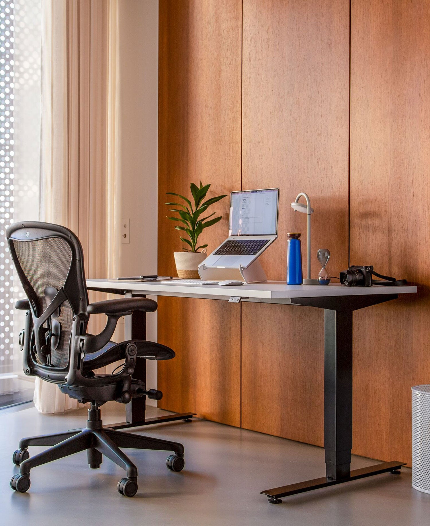 Oficina en casa con silla de oficina Aeron en grafito delante de un escritorio sit-stand Nevi con patas negras y superficie blanca y soporte para portátil Oripura.