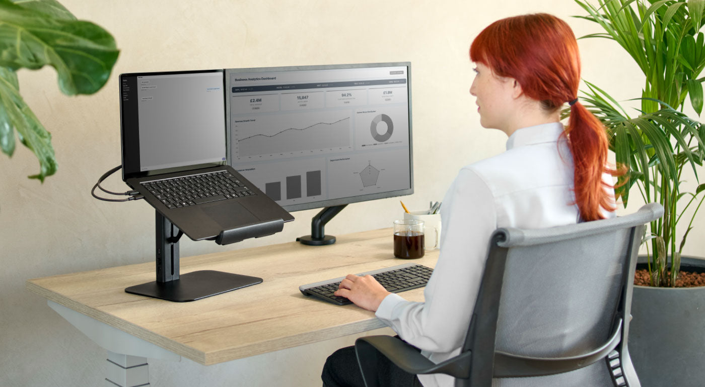 Una mujer utilizando una configuración de oficina en casa con un escritorio Nevi, una silla Setu y un soporte para portátil Lana.