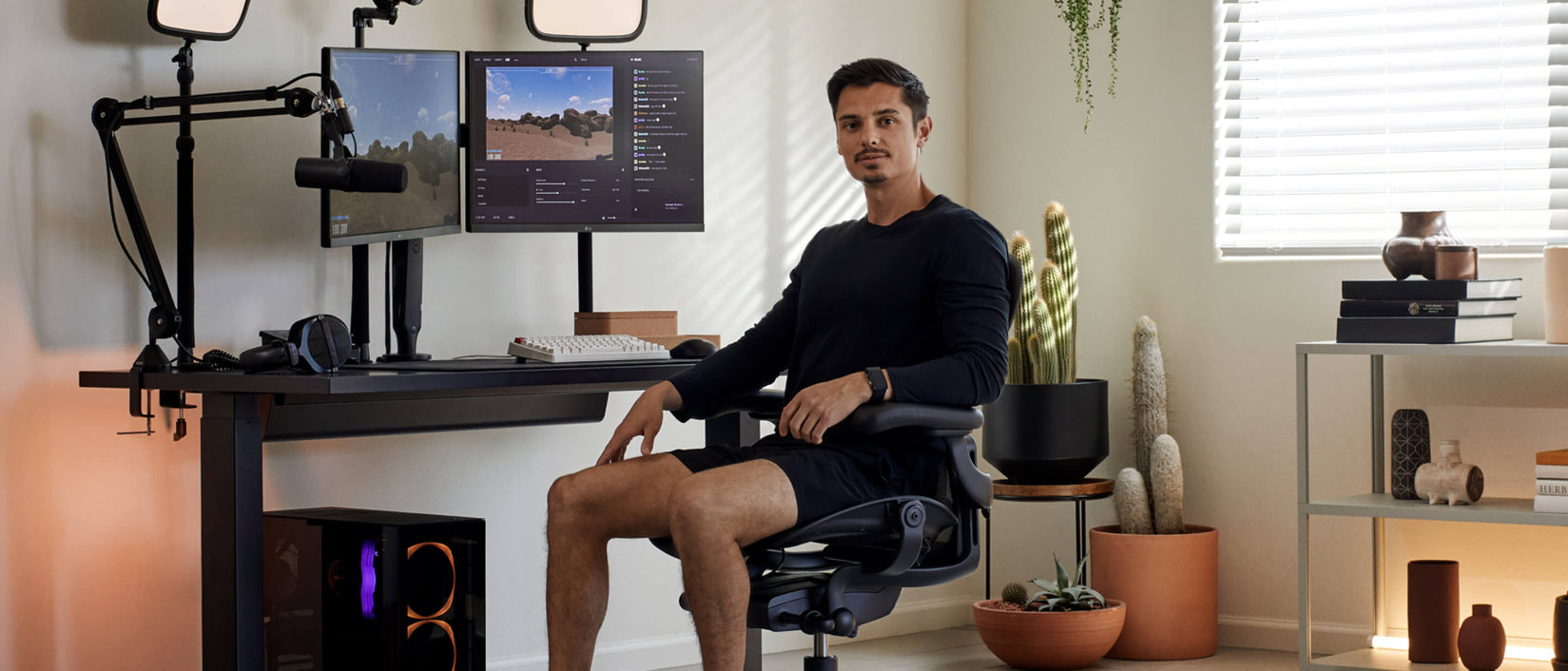 Foto del gamer Xaryu sentado frente a la cámara en una silla gaming Aeron en grafito con su equipo de gaming detrás, compuesto por un escritorio gaming Nevi y brazos para dos monitores Ollin.