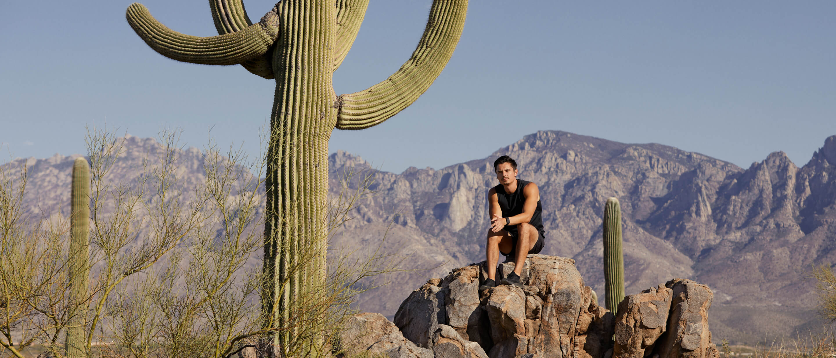 El jugador Xaryu sentado sobre unas rocas en un espacio rocoso y montañoso al aire libre, rodeado de grandes cactus.