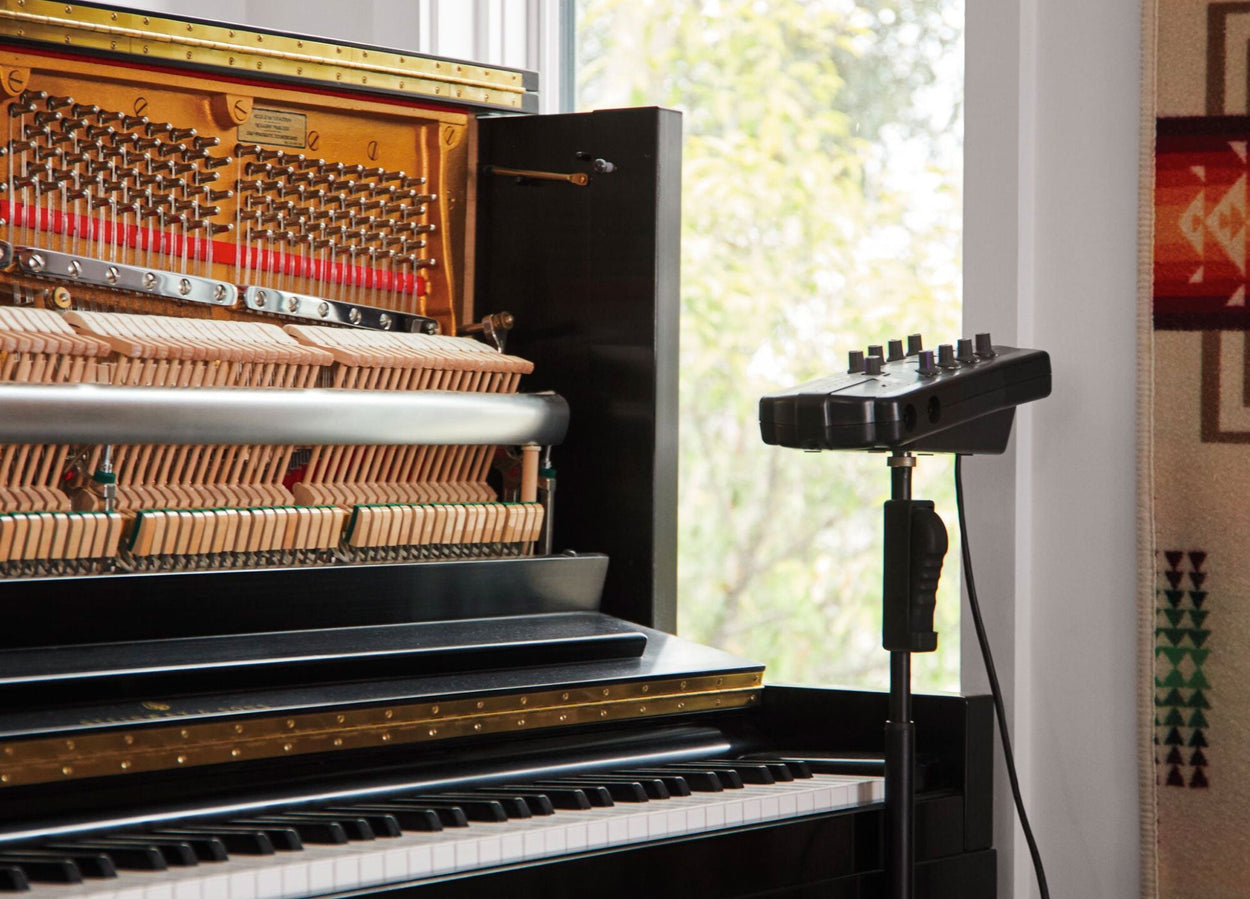 Un piano vertical con la parte delantera abierta y equipo de grabación de sonido junto a él.