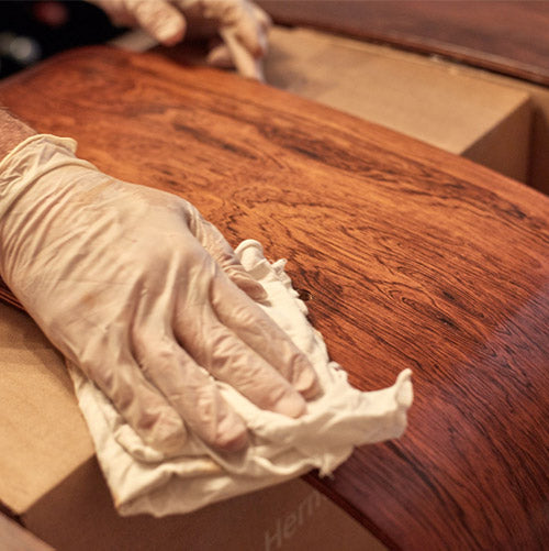 Primer plano de una mano enguantada puliendo chapa de madera.