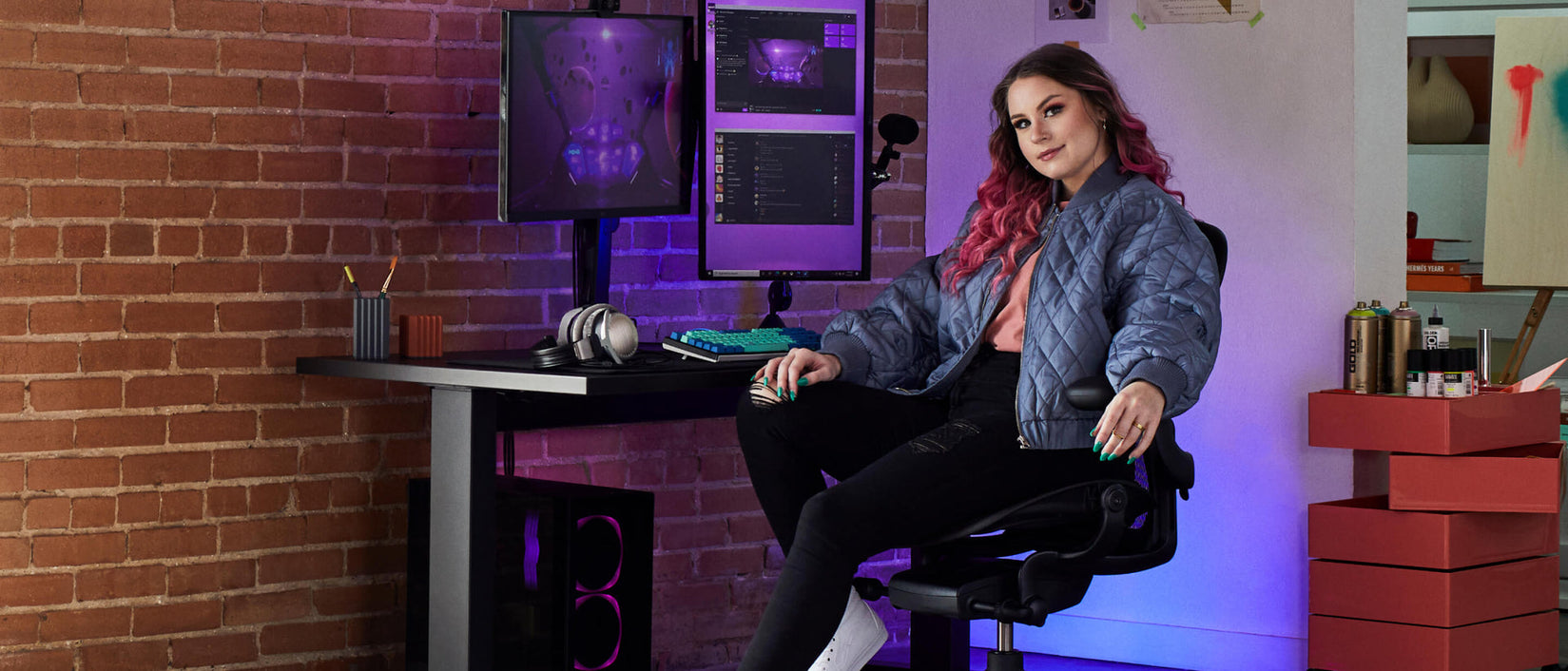 Foto de la jugadora Electra mirando a la cámara sentada en una silla gaming Aeron en negro ónix  delante de un escritorio gaming Nevi en negro con un monitor Ollin