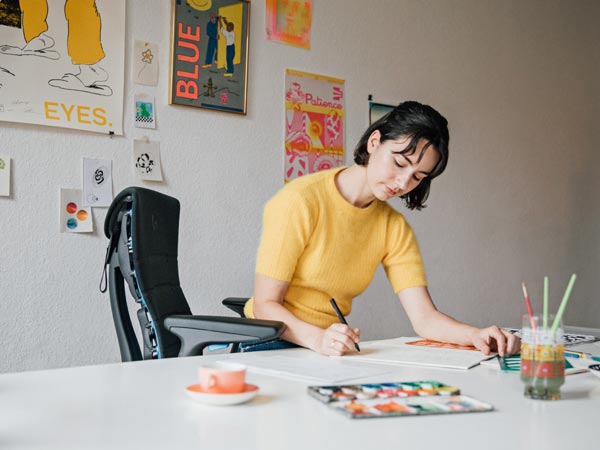 La ilustradora, pintora y autora Molly Rose Dyson trabajando en su estudio sentada en una silla gaming Embody en negro y azul cian