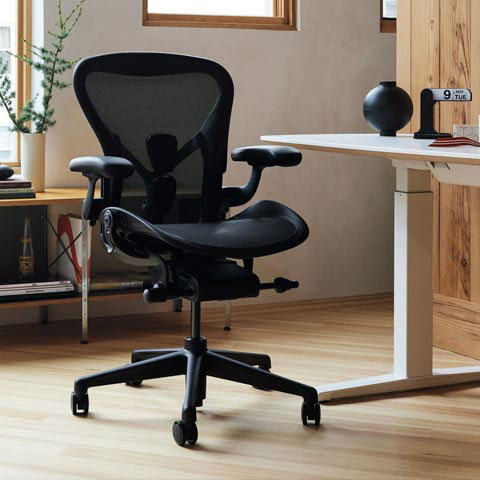 Silla de oficina Aeron en grafito en un entorno de oficina en casa con escritorio sit-stand Nevi con patas y superficie blancas.