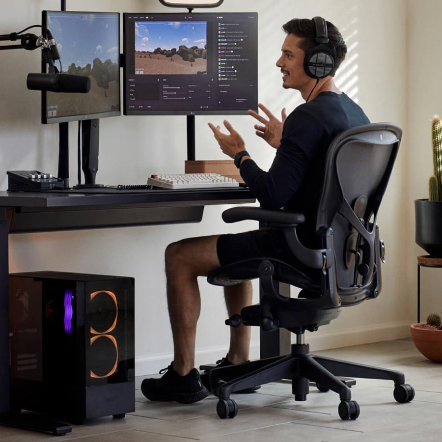 El jugador y streamer Xaryu en una configuración para gaming sentado en una silla para gaming Herman Miller Aeron con un escritorio para gaming Nevi de altura regulable en negro y dos monitores en brazos para monitor Ollin.