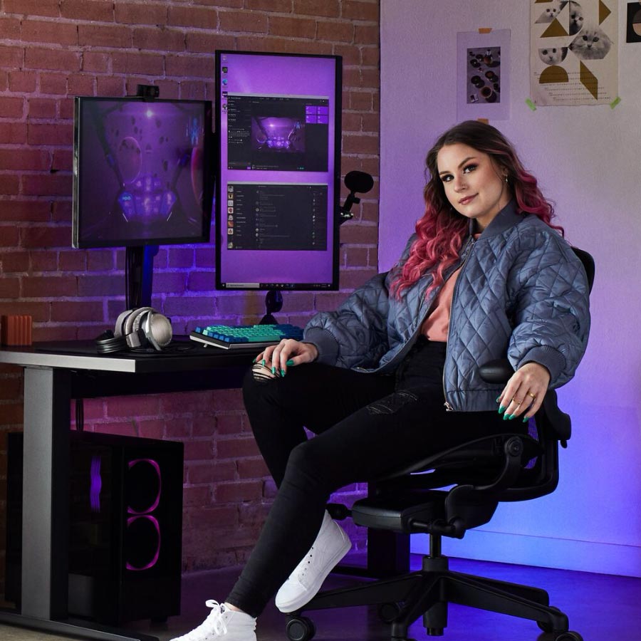 La famosa jugadora y entrenadora Electra sentada en un conjunto gaming que incluye una silla gaming Aeron de Herman Miller con un escritorio sit-stand Nevi en negro con dos monitores en brazos para monitor Ollin.