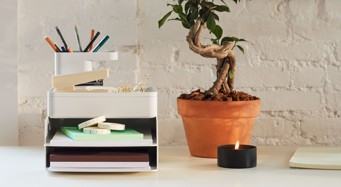 Un conjunto de accesorios de escritorio Formwork en gris hormigón junto a una planta y una vela sobre un escritorio.