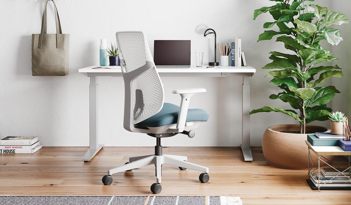 Una silla de oficina Verus blanca y azul de Herman Miller, colocada delante de un escritorio de pie Nevi blanco.