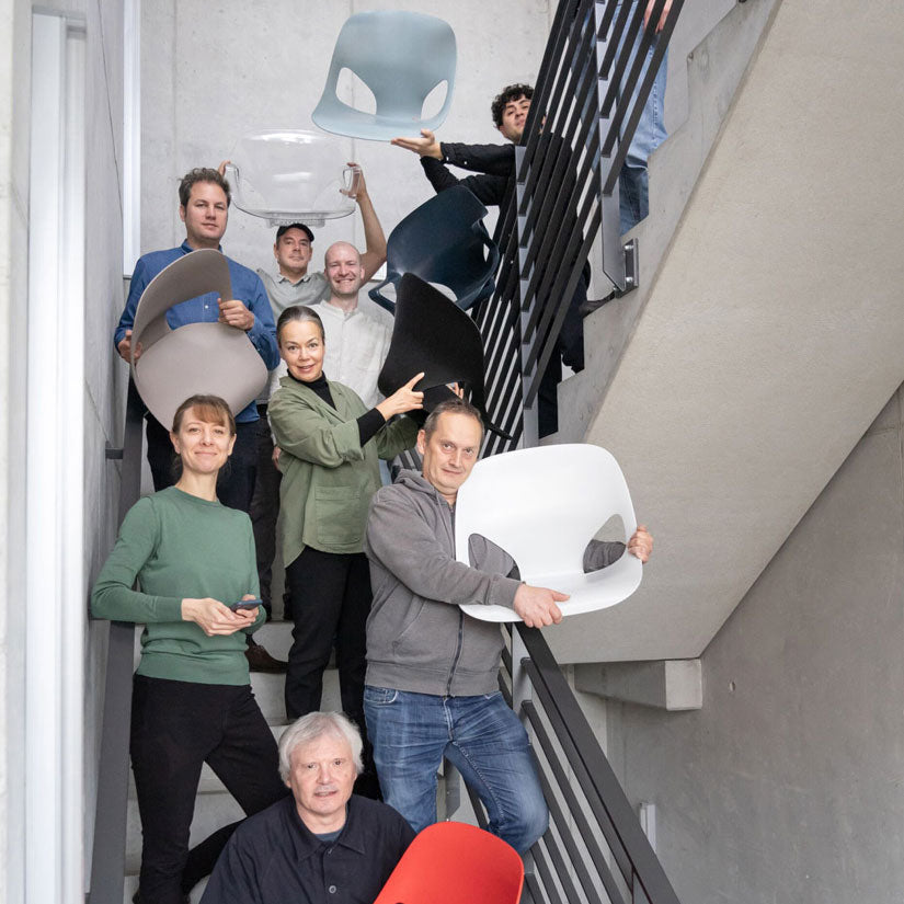 Fotografía de los miembros del equipo de diseño de Studio 7.5 en una escalera, algunos de ellos sosteniendo diferentes partes de la silla Herman Zeph que ellos mismos han diseñado.