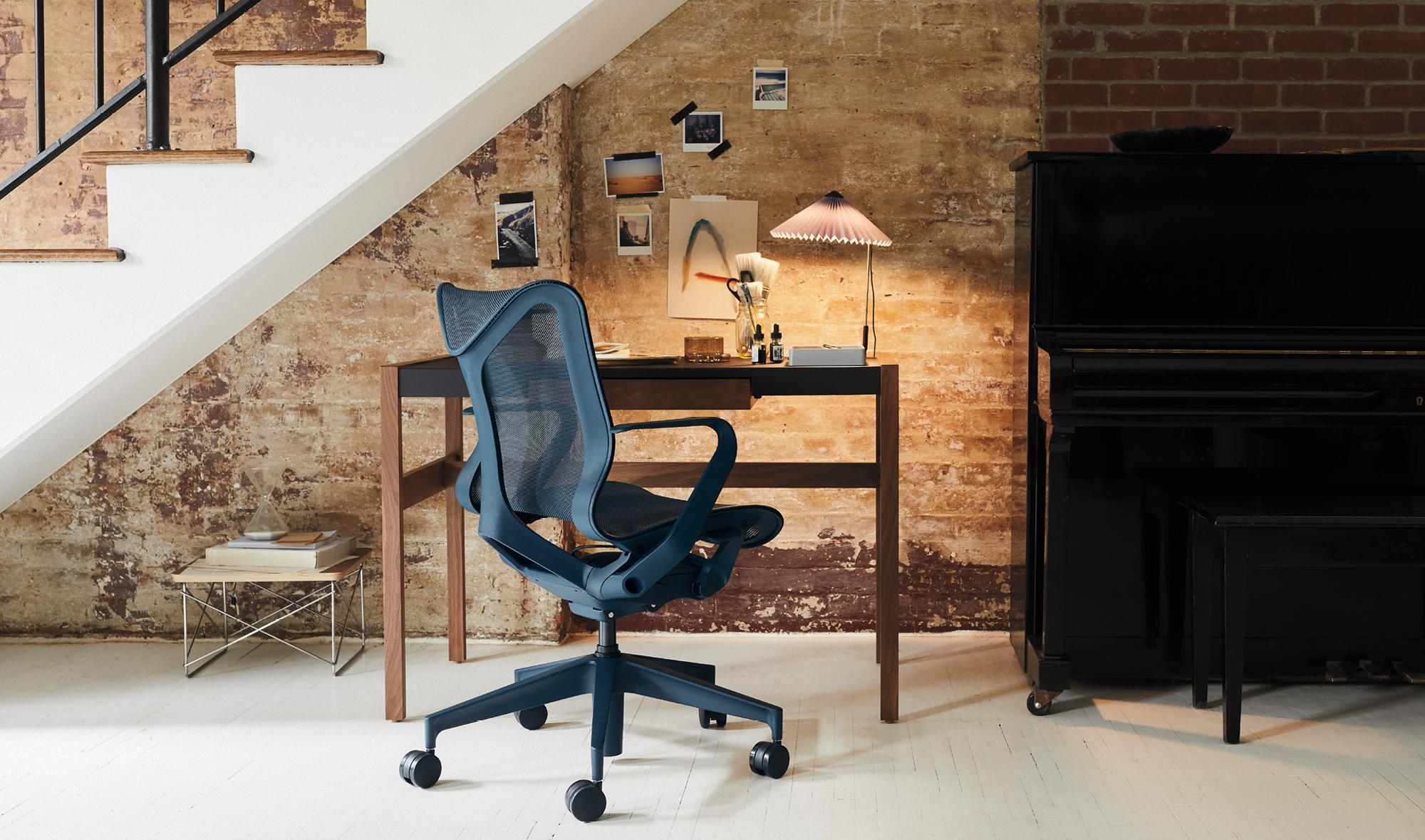 Una silla de oficina azul Herman Miller Cosm colocada delante de un escritorio y debajo de una escalera en un entorno doméstico.